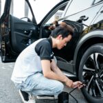 Asian man using a pump to inflate a car tire on a city street in Ho Chi Minh City, Vietnam.