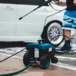 A person washing a white car with a pressure washer in outdoor setting, showcasing vehicle maintenance.