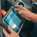 A mechanic uses a diagnostic tablet inside a car for vehicle analysis.